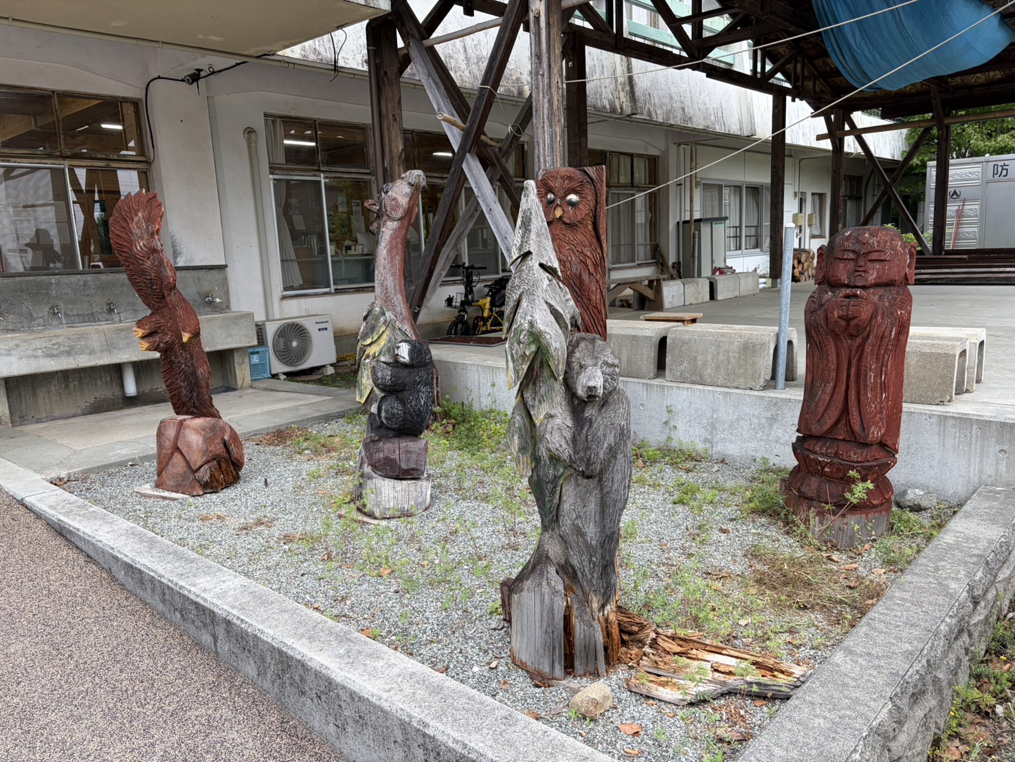 有人休憩所の前に展示されているチェーンソーアートの作品群。鷲・フクロウ・人物など4体が並んでいる。