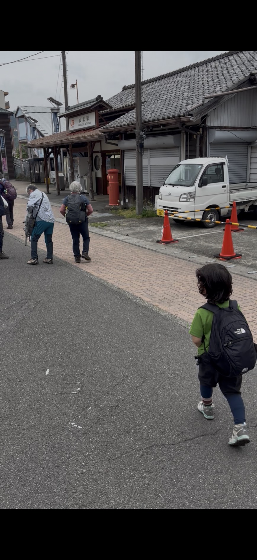 山北駅前の街並みを歩く子供と登山者たち。昔ながらの駅舎と赤いポストが見える。