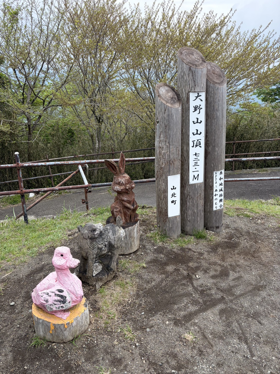 大野山の山頂標識（標高723m）。標識の傍にウサギとアヒルのチェンソーアートが飾られている。