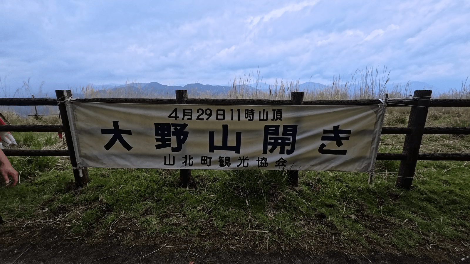 「4月29日11時山頂 大野山開き 山北町観光協会」と書かれた横断幕。背景に曇り空と山並みが広がる。