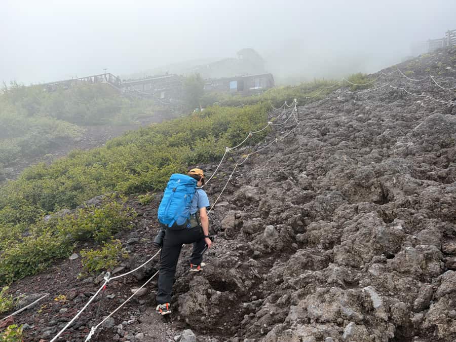 ロープが張られた岩まじりの斜面を、ザックを背負って登っていくところ(七合目付近)