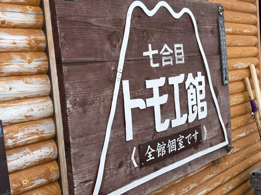 丸太づくりの壁に掛かる「七合目 トモエ館」の木製看板。七合目には山小屋が次々と現れる