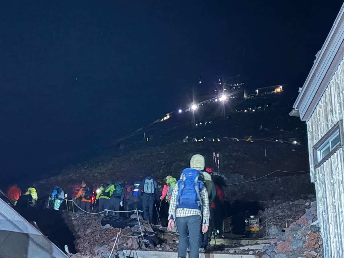 深夜の登山道。斜面の上に向かってヘッドライトの光が数珠つなぎに続いている