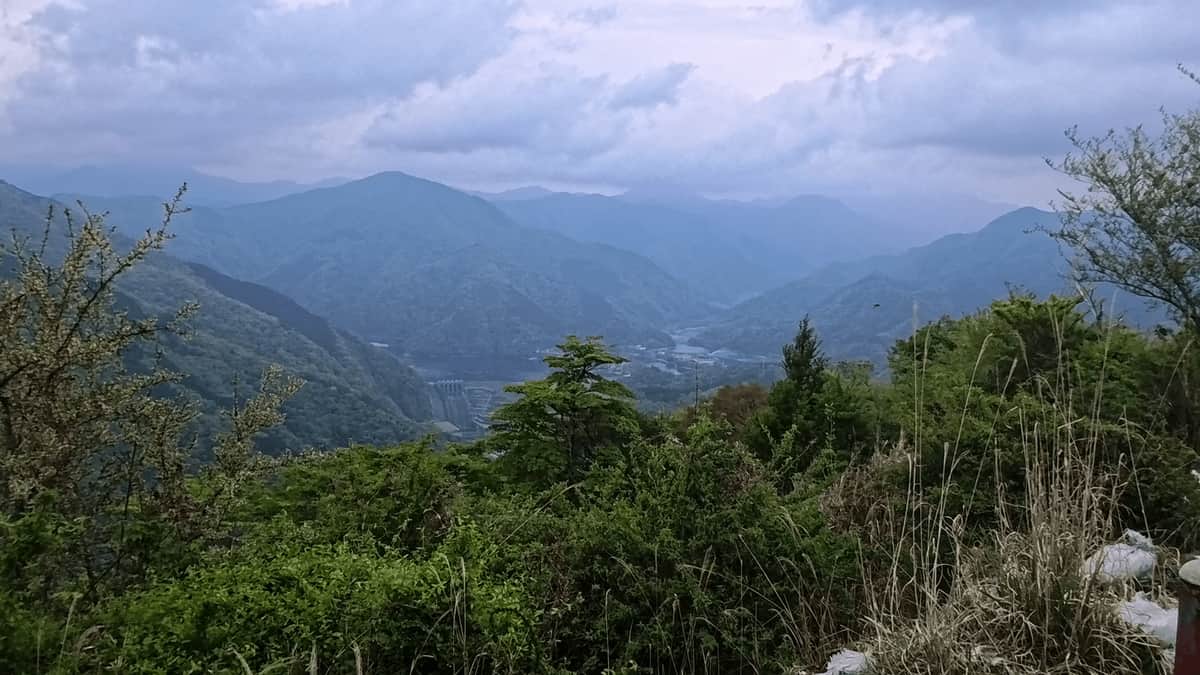 大野山山頂付近から見た丹沢湖方面の眺め。重なり合う山並みの向こうに、湖と曇り空が広がる。